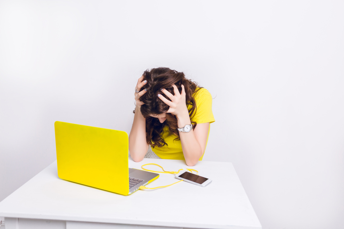 Femme brune avec un haut jaune triste devant PC jaune